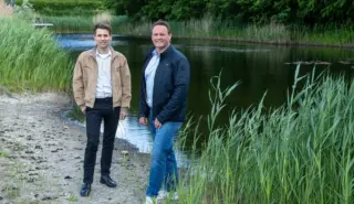Twee medewerkers staan voor een rivier